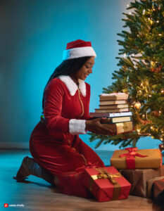 A young girl holds a stack of books near a decorated Christmas tree